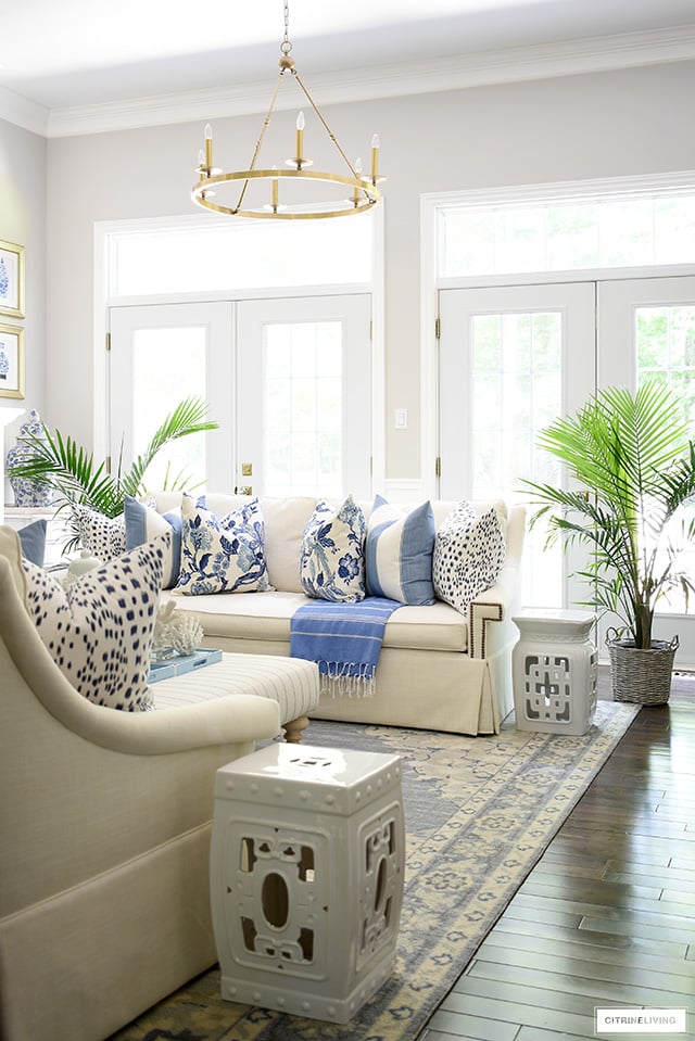 Summer living room decor with blue and white pillows, rug and palm plants.