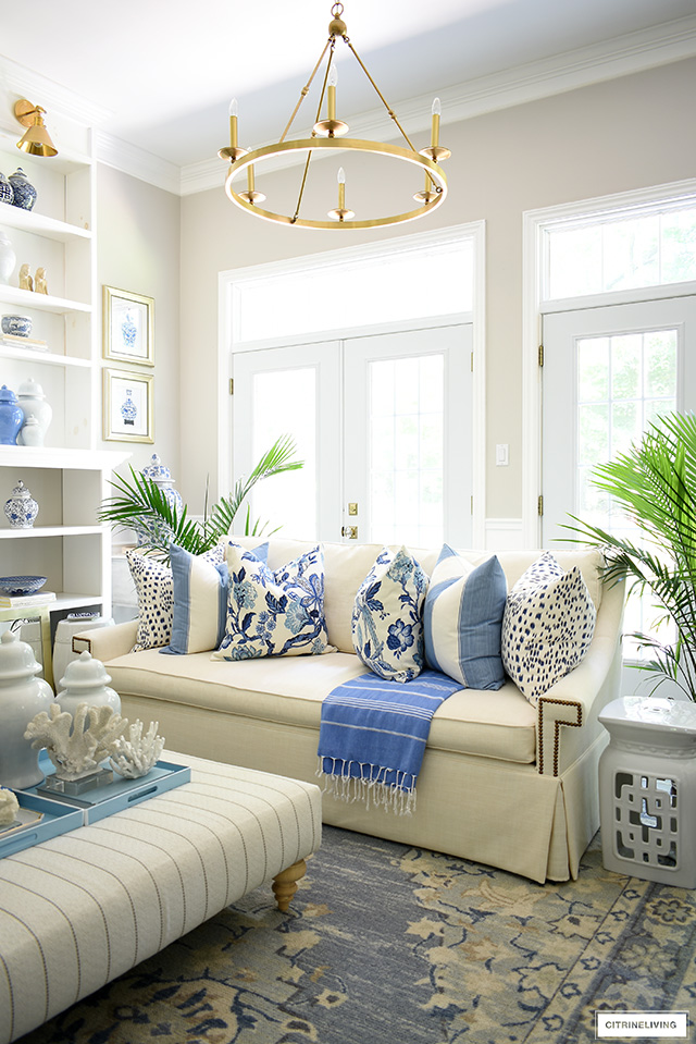 A collection of hamptons-inspired blue and white print pillows styled on a white sofa for summer.