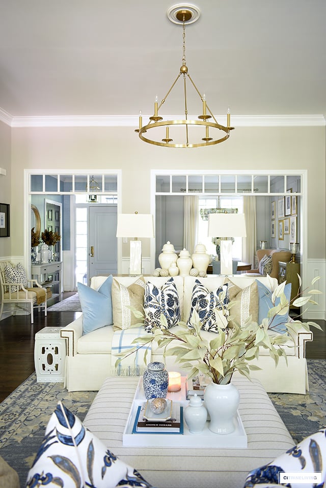 Living room sofa styled with designer throw pillows, ottoman/coffee table styled with white trays and seasonal accents.