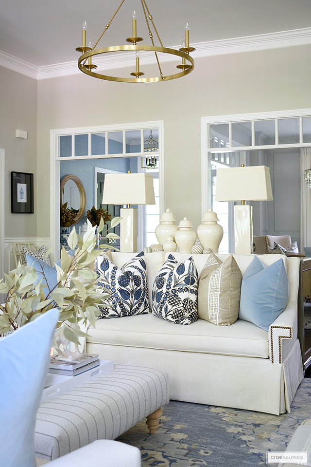 Living room styled for fall with beautiful designer pillows in blues and warm neutrals, on a white sofa.