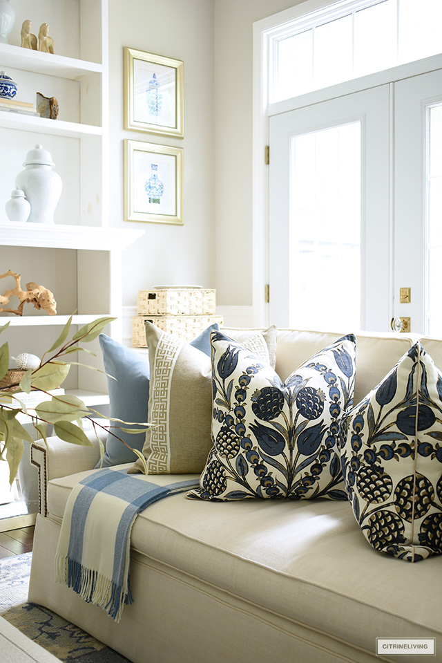 Beautiful designer pillows styled on a white sofa with a plaid throw for fall.