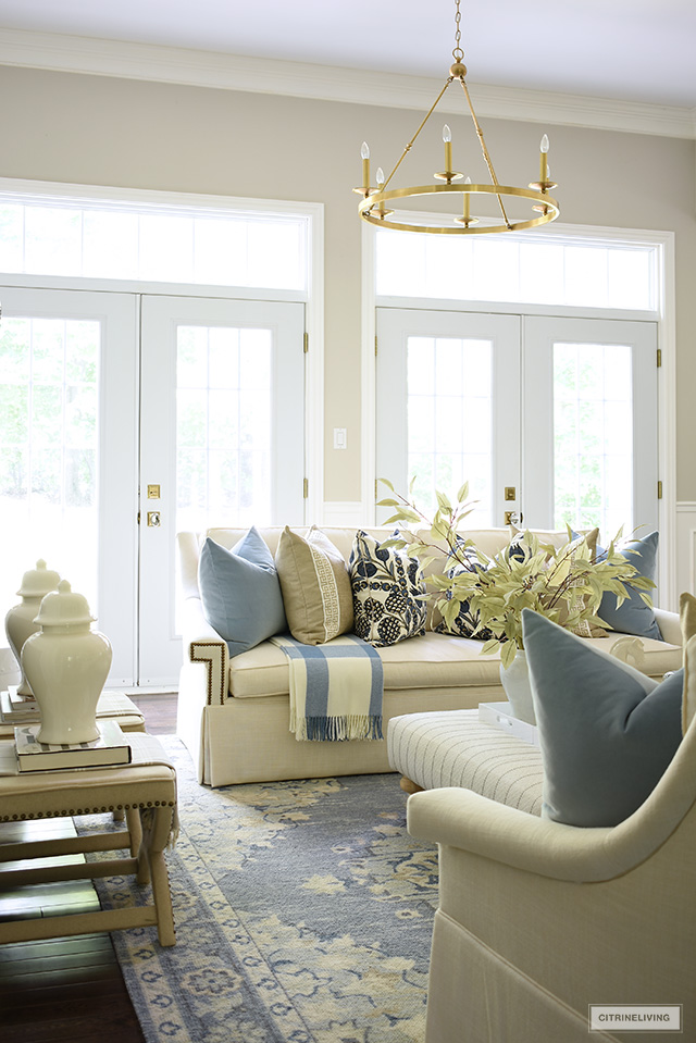 White living room sofa with beautiful designer pillows and a plaid throw, in a blue and warm neutral color palette.