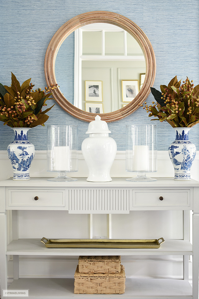 Console table styled for fall with a symmetrical display - faux foliage flanking glass hurricanes and a simple ginger jar.