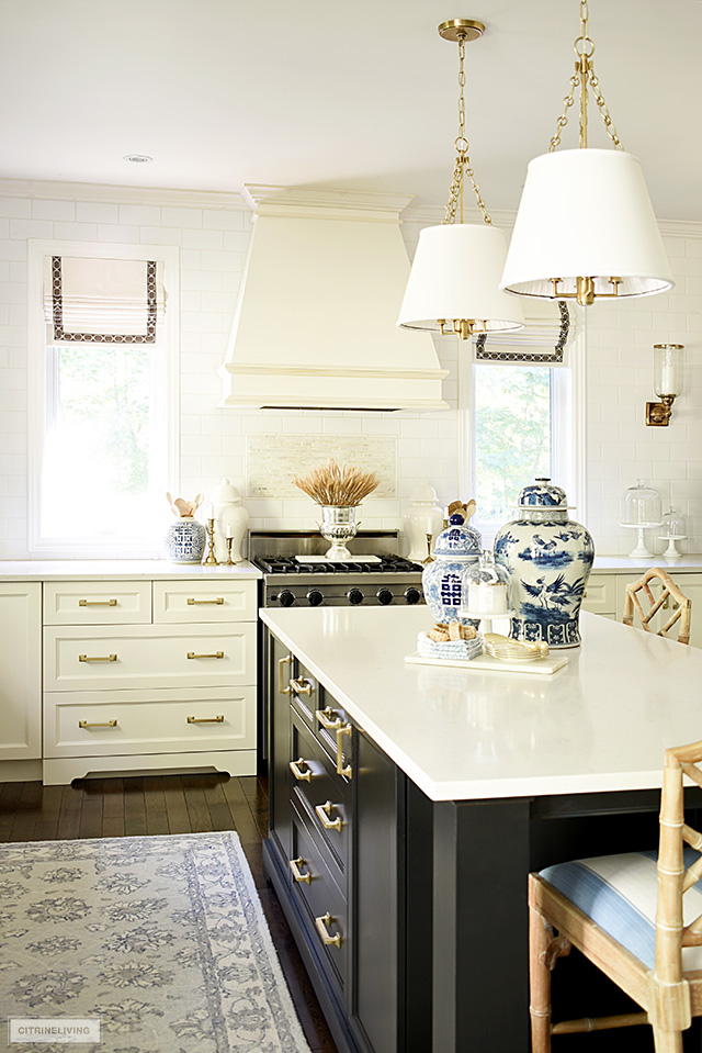 White kitchen with black island styled for fall with blue and white ginger jars and faux wheat styled in a champagne bucket on the stove, flanked by ginger jars and candlesticks.