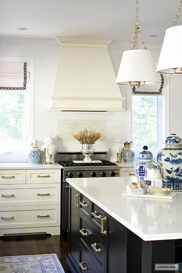 Kitchen decorated for fall with a dried wheat arrangement on the stove, ginger jars and candlesticks flanking the stove and blue and white ginger jars on the island.