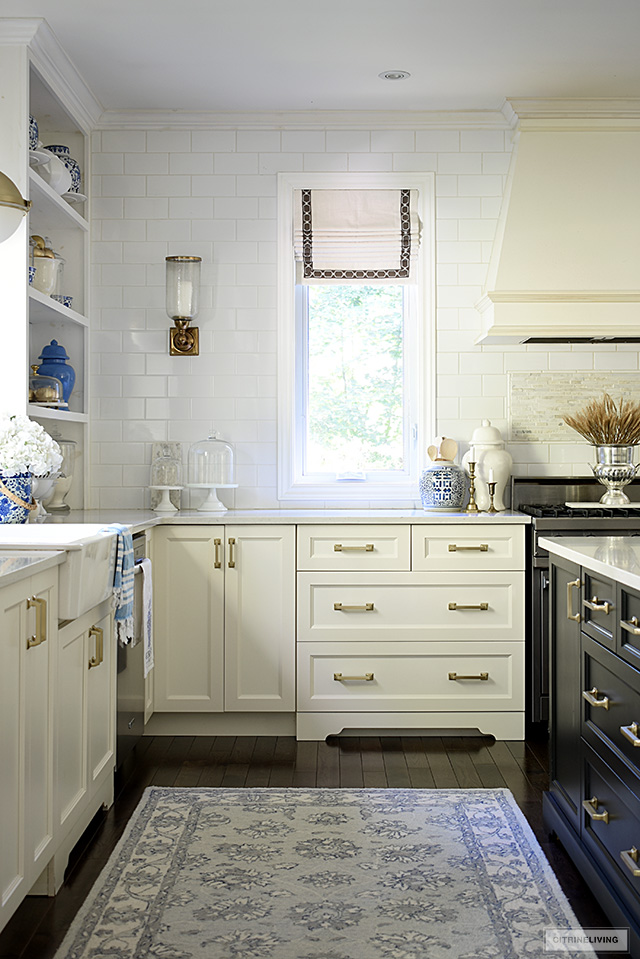 Corner of a kitchen with ivory cabinets, brass hardware, blue an white ginger jars and a dried wheat arrangement for fall.