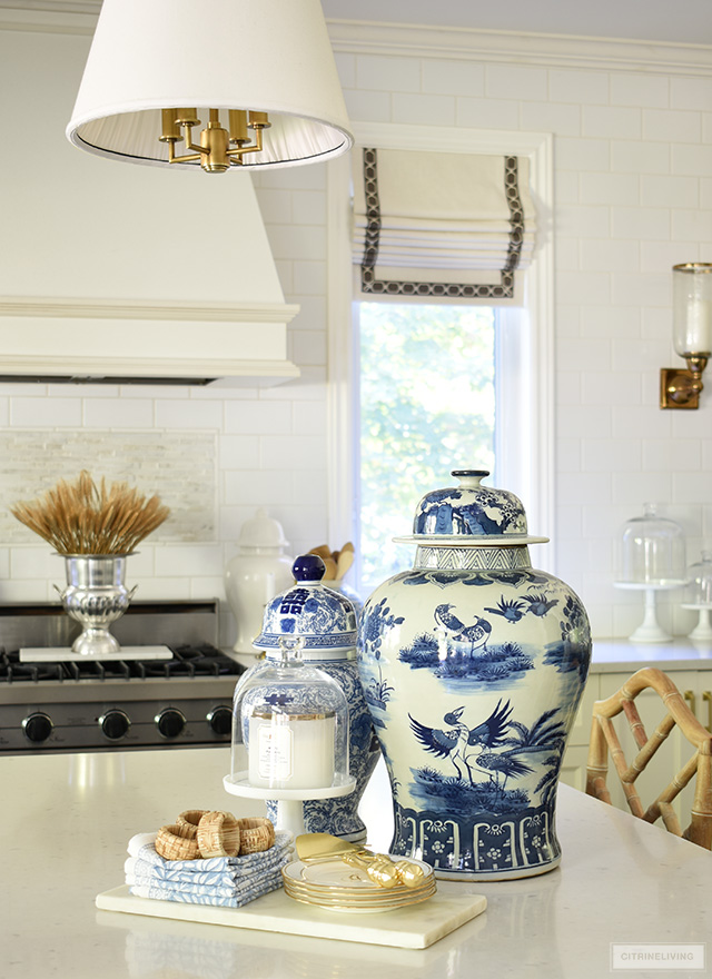 Blue and white ginger jars styled on a kitchen island with a marble tray and dishes. A dried wheat arrangement is styled on the stove.