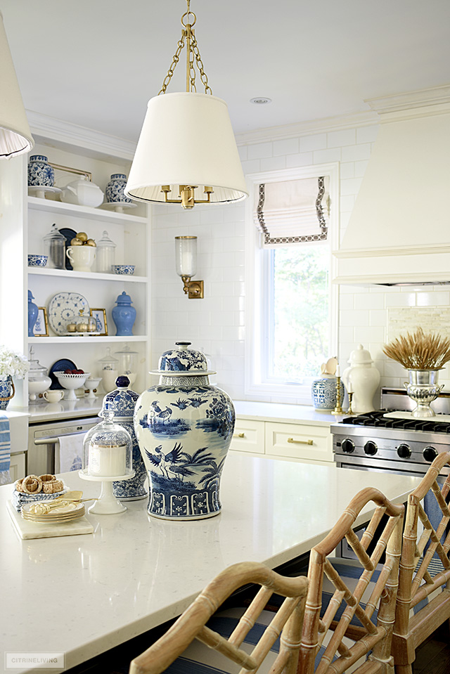 Kitchen decorated for fall with ginger jars displayed on an island, open shelves with blue and white dishes, and seasonal accents.