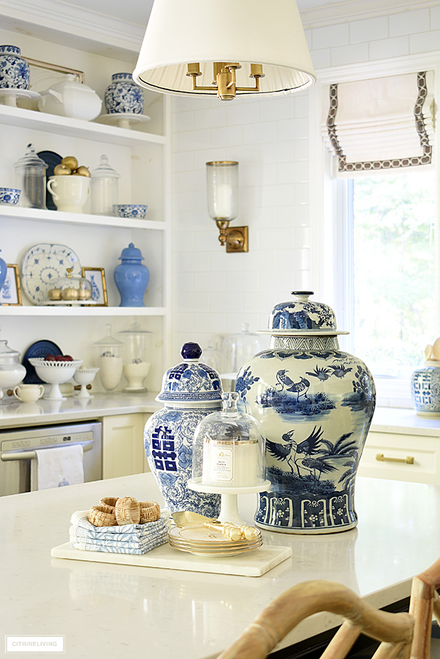 Ginger jars styled on a kitchen island with a marble tray, gold dishes, blue and white napkins and cane napkin rings.