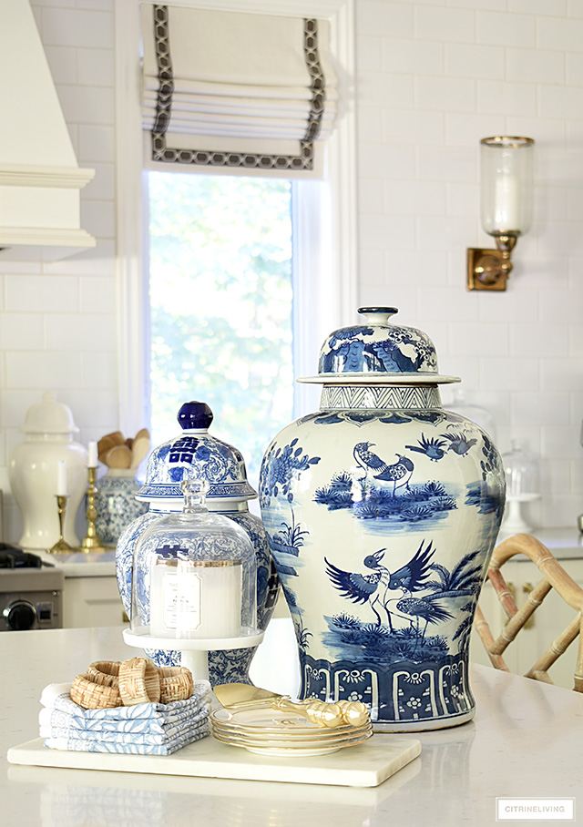 Kitchen island styled with blue and white ginger jars, marble tray, gold dishes, blue napkins and woven napkin holders.