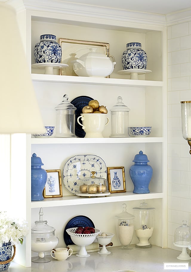 Open kitchen shelves with blue and white chinoiserie bowls, ginger jars and platter, styled with faux gold apples for fall.