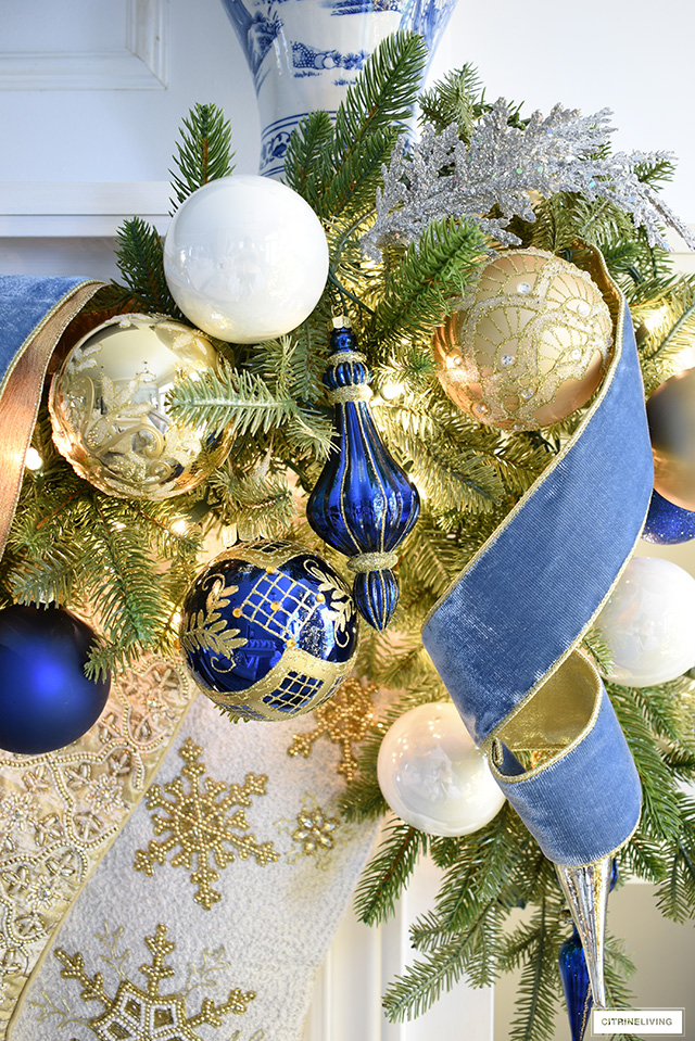 Stunning blue, white an gold Christmas decorations on a green garland with blue velvet ribbon.