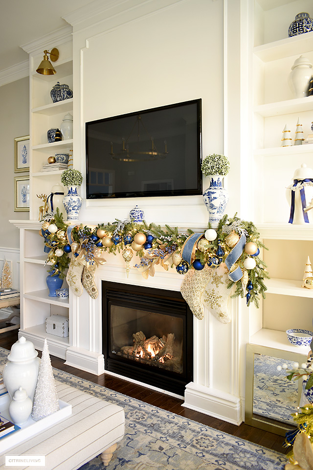 Holiday decorated mantel with swagged green garland decorated in gorgeous blue and gold decorations and ribbon.