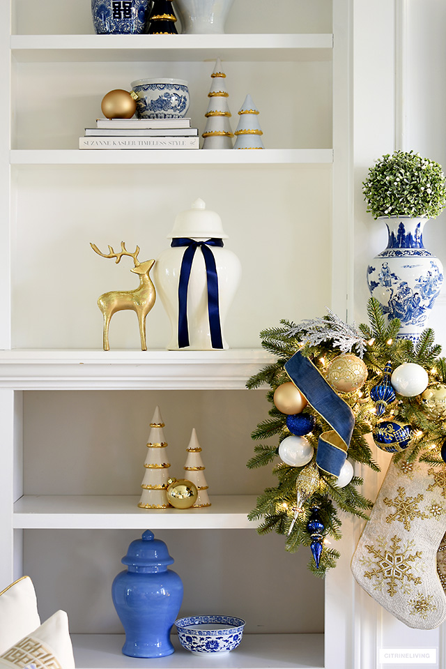 Bookshelf decorated for Christmas with simple blue white and gold decor - ceramic Christmas trees with gold edging gold reindeer and ginger jars.