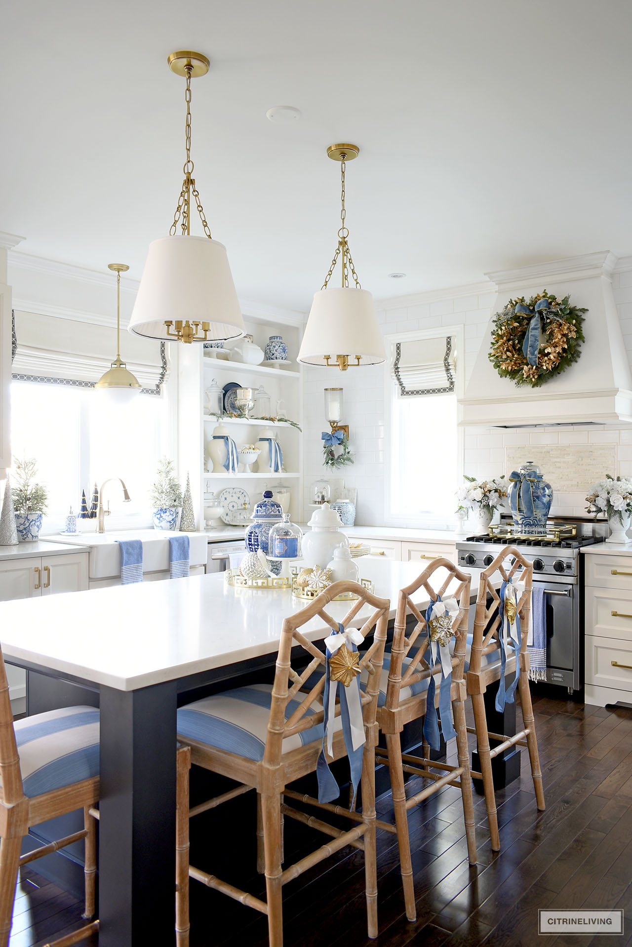 Kitchen decorated for Christmas with blue and gold and greenery touches throughout. Island barstools are styled with blue and white ribbons and gold ornaments tied on the back.
