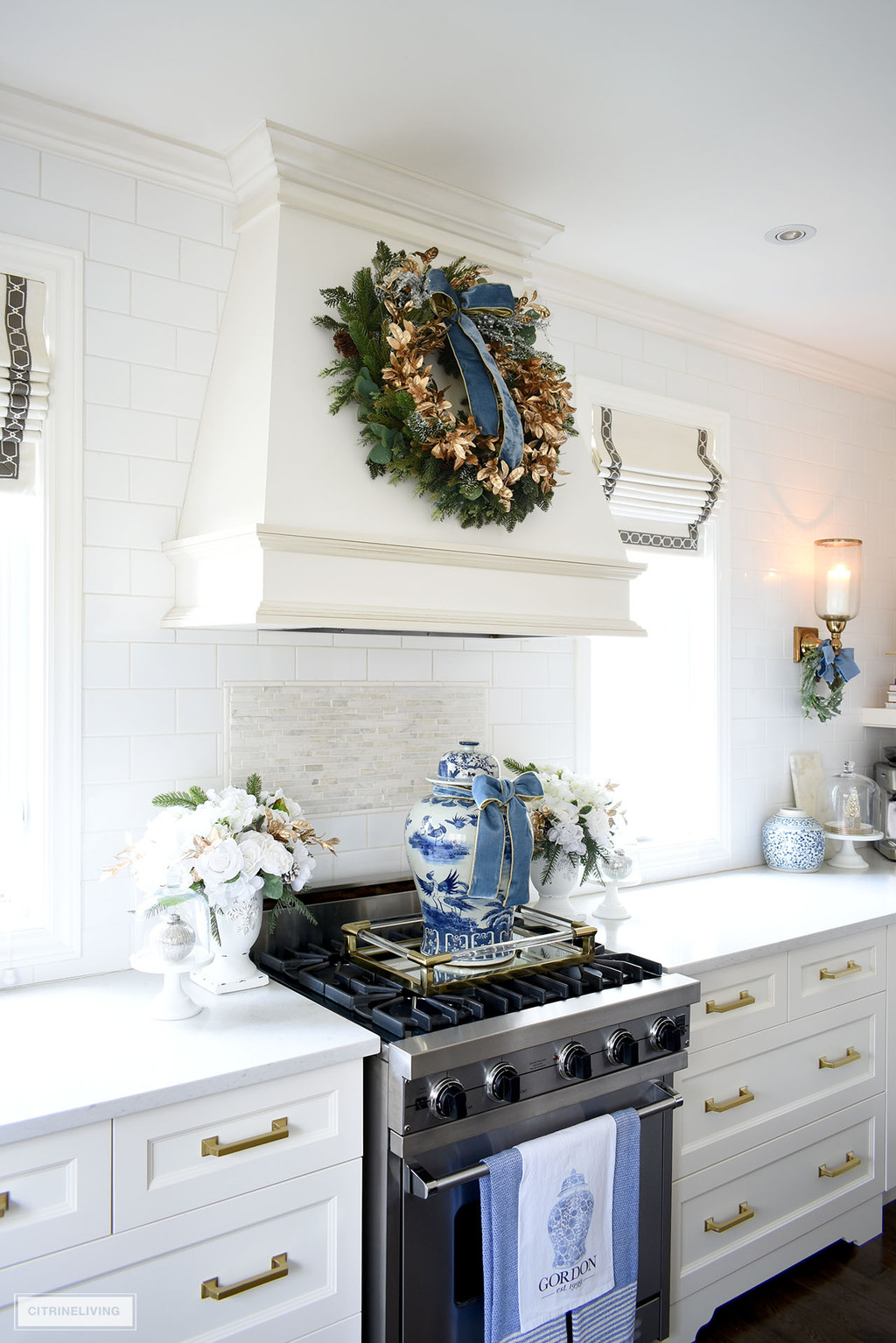 Kitchen stove styled for Christmas with a blue and white ginger jar, floral arrangements and a green and gold wreath hung on the hood above.