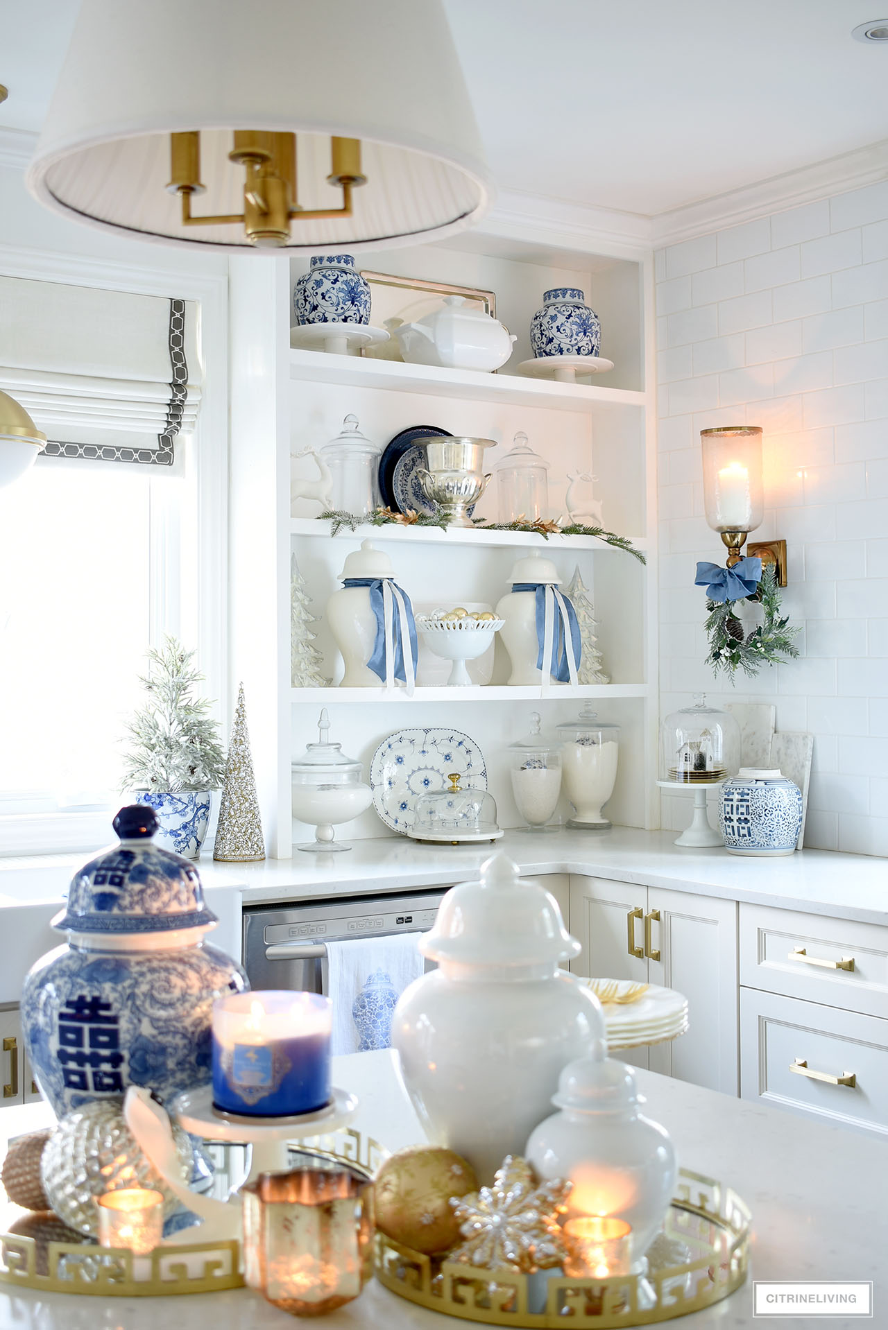 Open kitchen shelves styled for Christas with blue and white pieces, glass apothecary jars, white ceramic pieces and a few simple Christmas touches in white, gold and green.