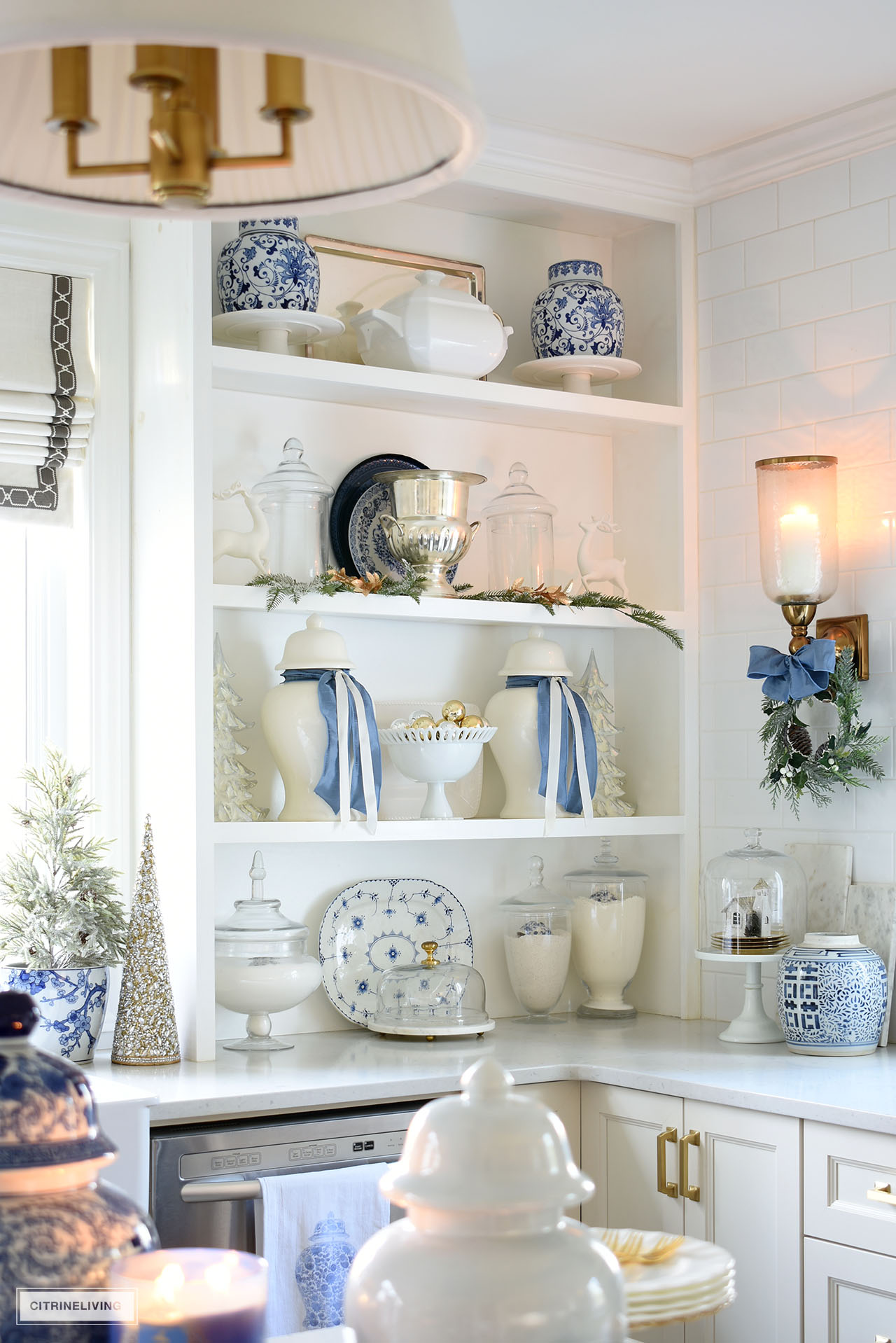 Open kitchen shelves decorated for Christmas with blue and white, greenery and gold accents.