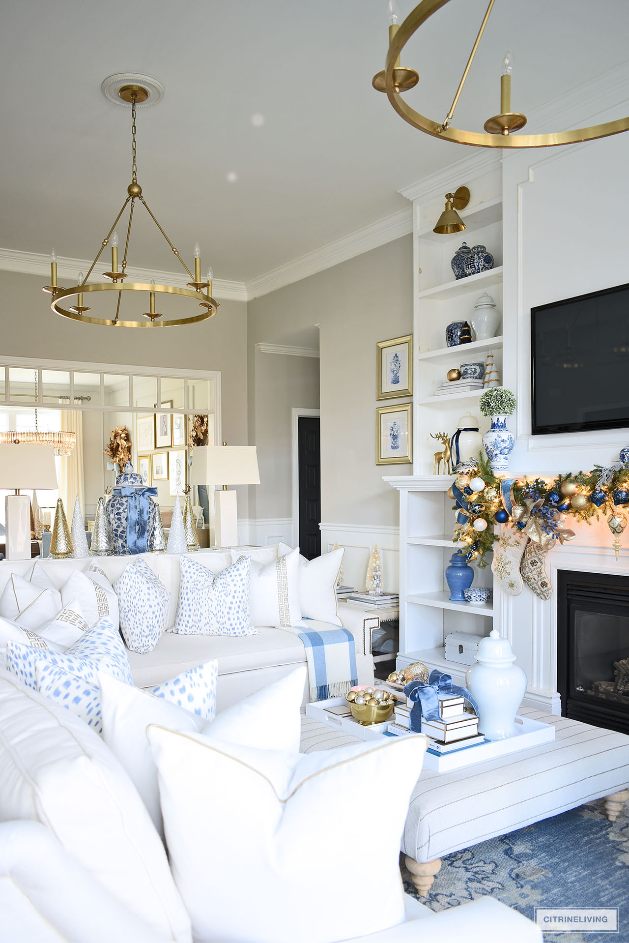 Living room styled for Christmas with white sofas, white, blue and gold pillows, garland with blue and gold ornaments and ribbon.