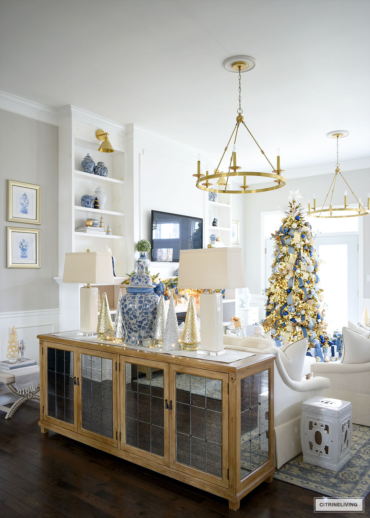 Living room with brass chandeliers, mirrored buffet with lamps, mercury glass christmas trees, large ginger jar in the center.