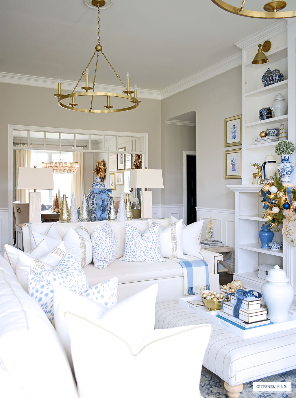 Blue and gold decorated christmas living room styled with white sofas with white, gold and blue pillows. 
