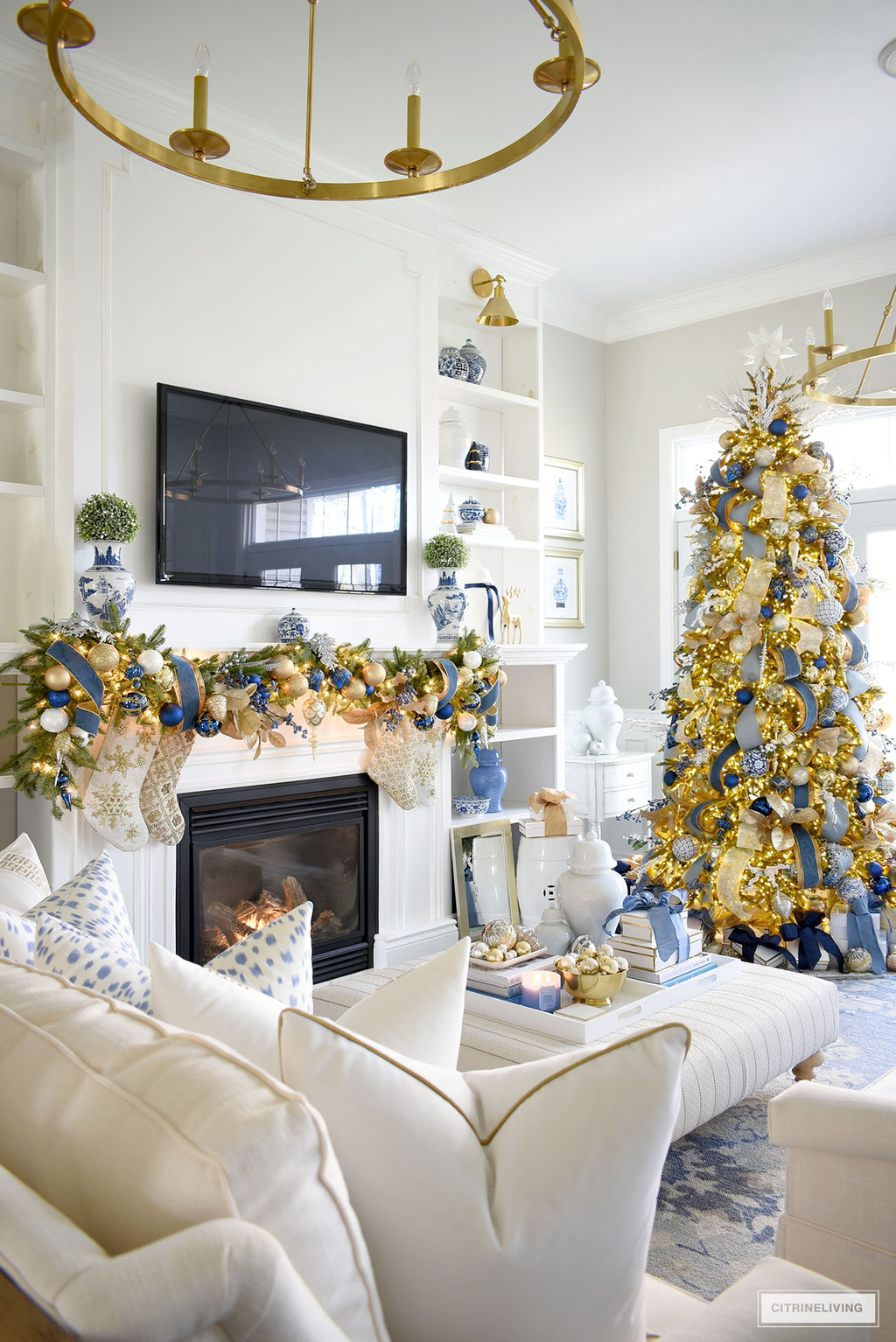 Gorgeous Christmas living room with blue and gold decorated tree and garland, blue, white and gold Christmas decor on bookshelves and ottoman.
