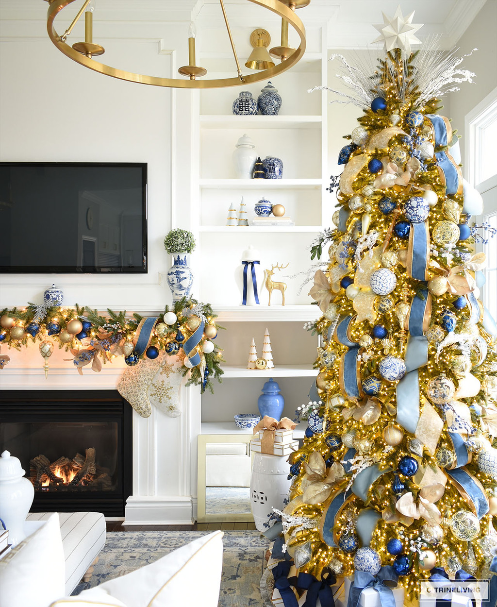 Beautiful blue and gold Christmas tree standing in front of builtin bookshelves styled with blue, white and gold holiday decor.