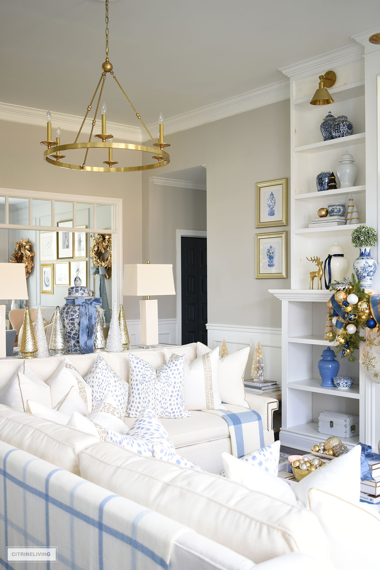 Christmas decorated living room featuring white sofas, white pillows with gold details. 