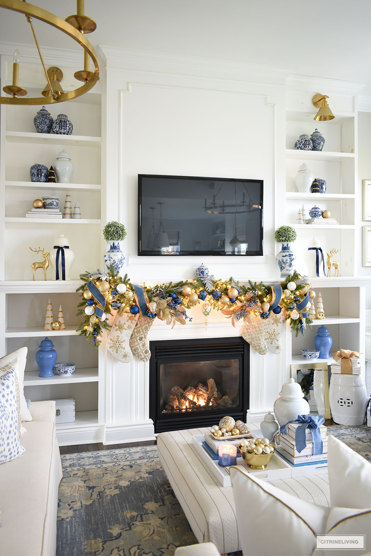 Living room bookshelves and fireplace decorated for Christmas with blue and gold acessories and garland 