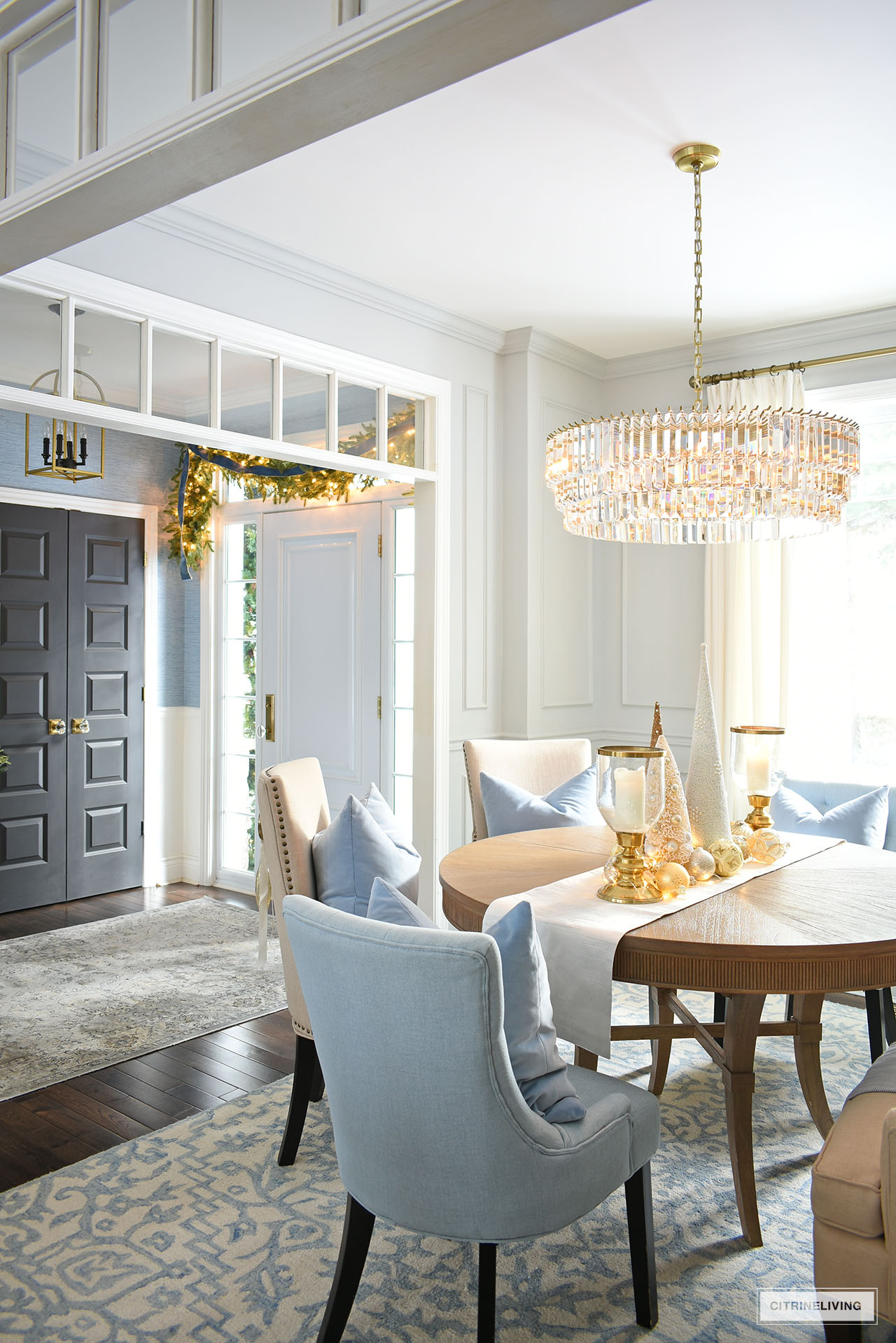Dining room styled for Christmas with a centerpiece white and gold trees, ornaments and glass hurricanes.