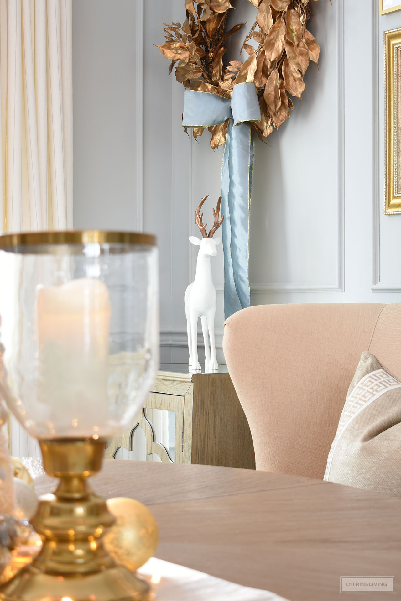 Dining room decor with a gold wreath hanging above a mirrored cabinet styled with a simple white and gold reindeer.