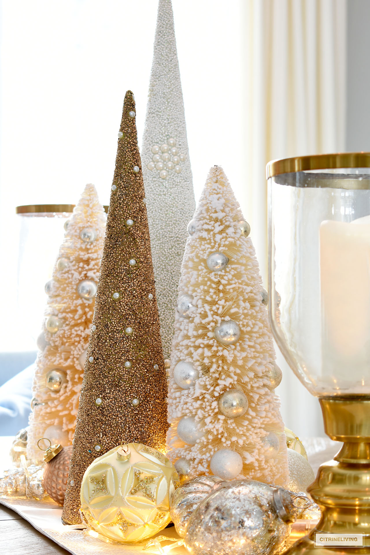 Christmas centerpiece with gold and ivory beaded trees, bottlebrush trees, ornaments and glass hurricanes.