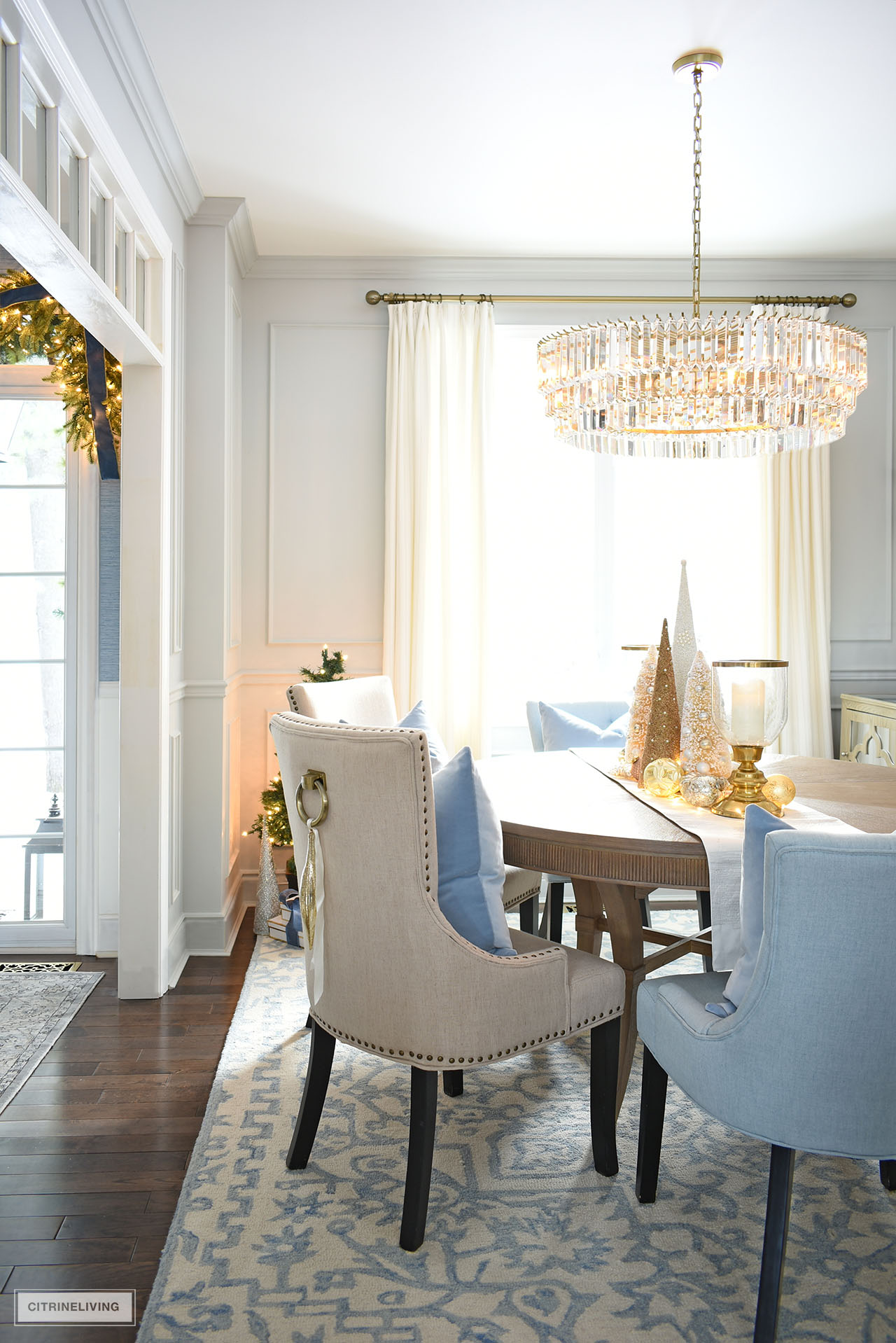 Dining room decorated for Christmas with simple decor and a centerpiece with white and gold tabletop trees and ornaments.