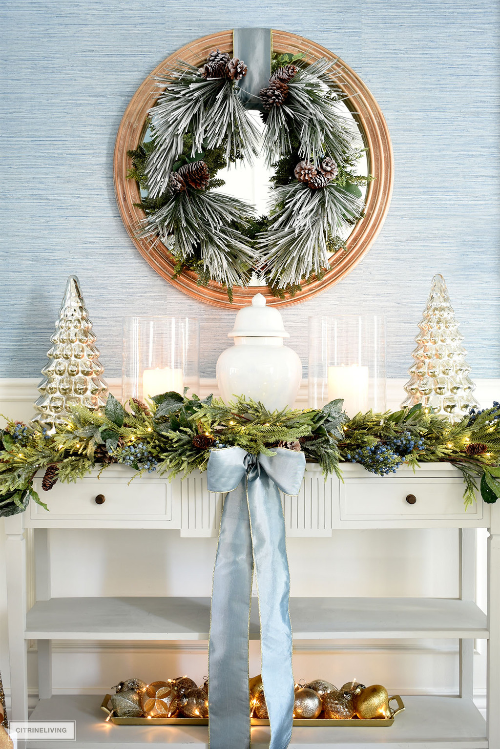 Elegant Christmas decor styled on a grey console table with beautiful ginger jar, hurricane lanterns, mercury glass trees.
