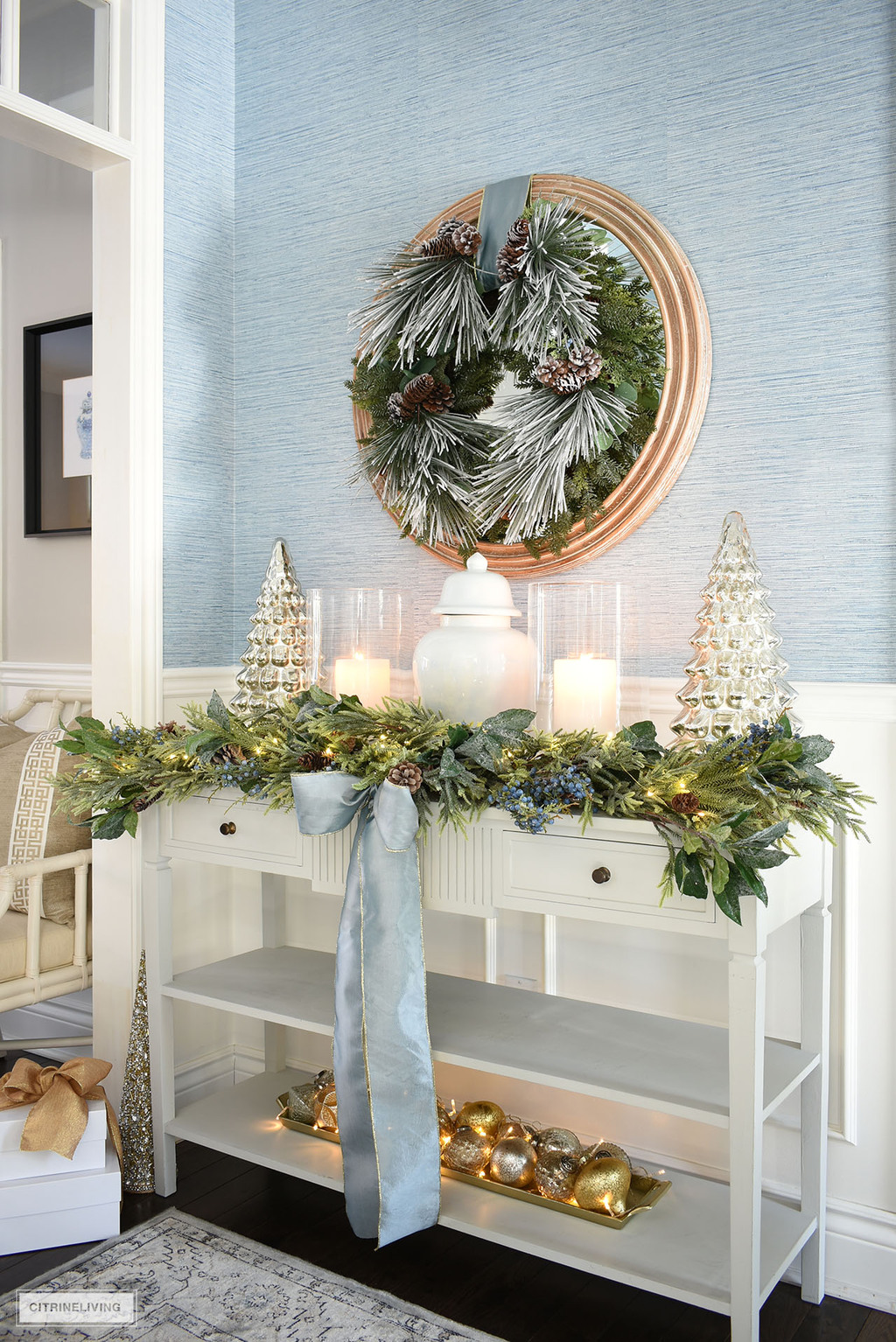 Gorgeous Christmas entryway console table styled with alush green wreath hanging above and garland on the table. 