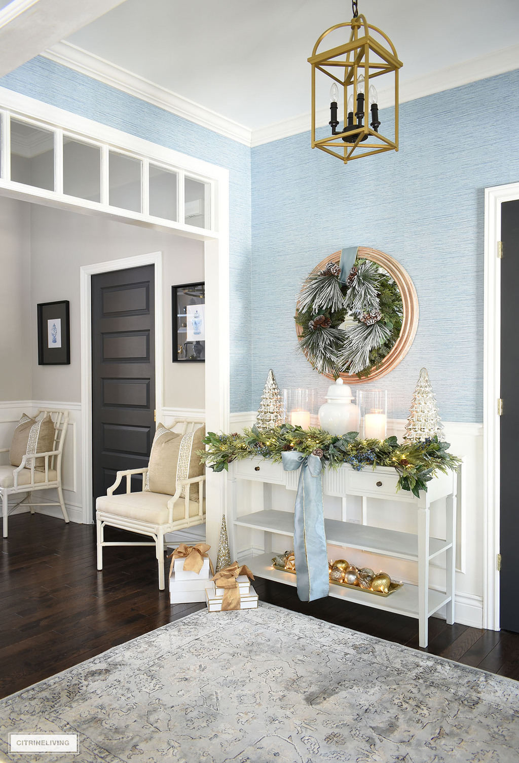 Elegant christmas entryway decorated with greenery, blue ribbon and gold and silver decor.