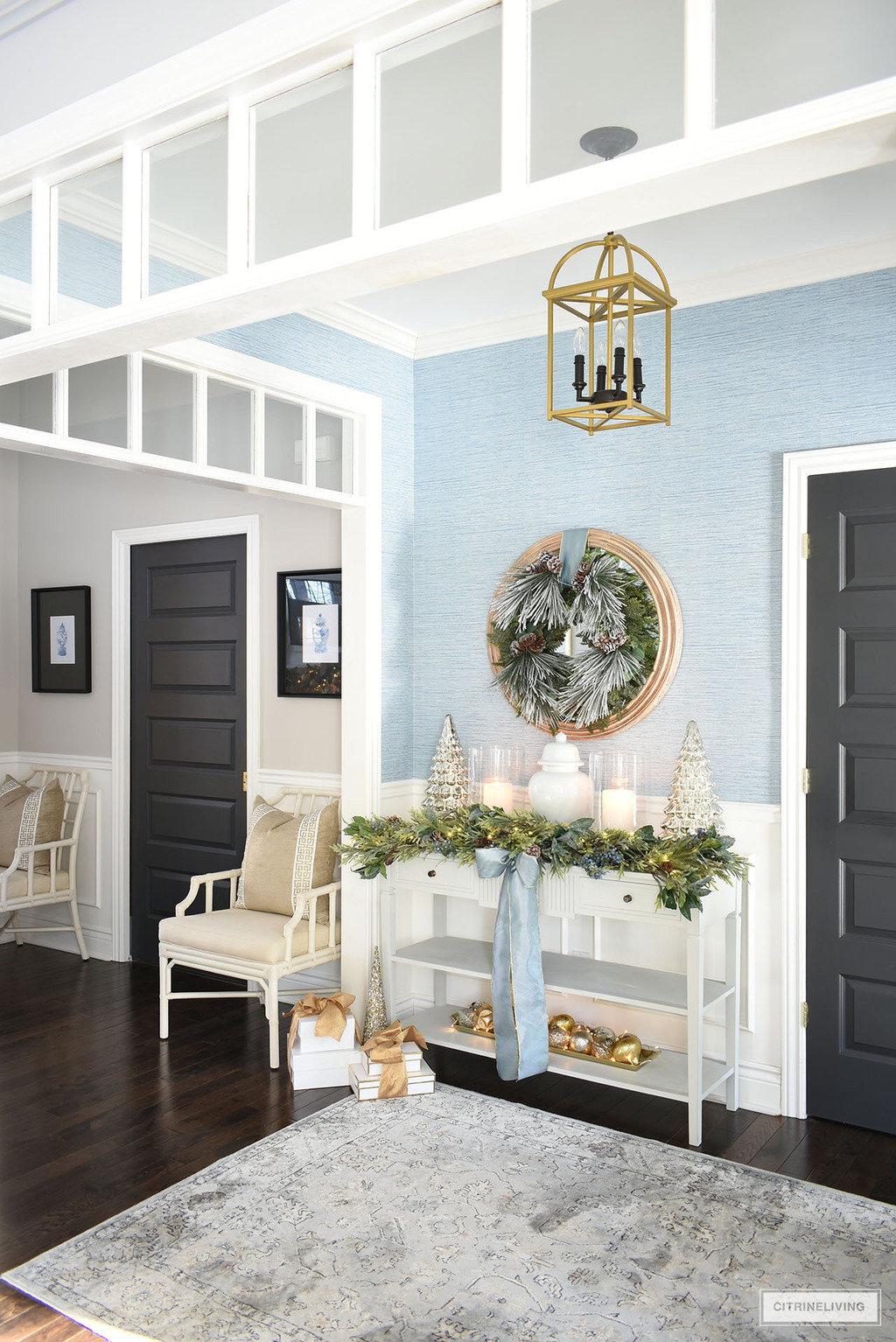 Entryway decorated for Christmas with green garland and wreath, mercury glass trees and silver and gold ornaments, accented with blue ribbon.