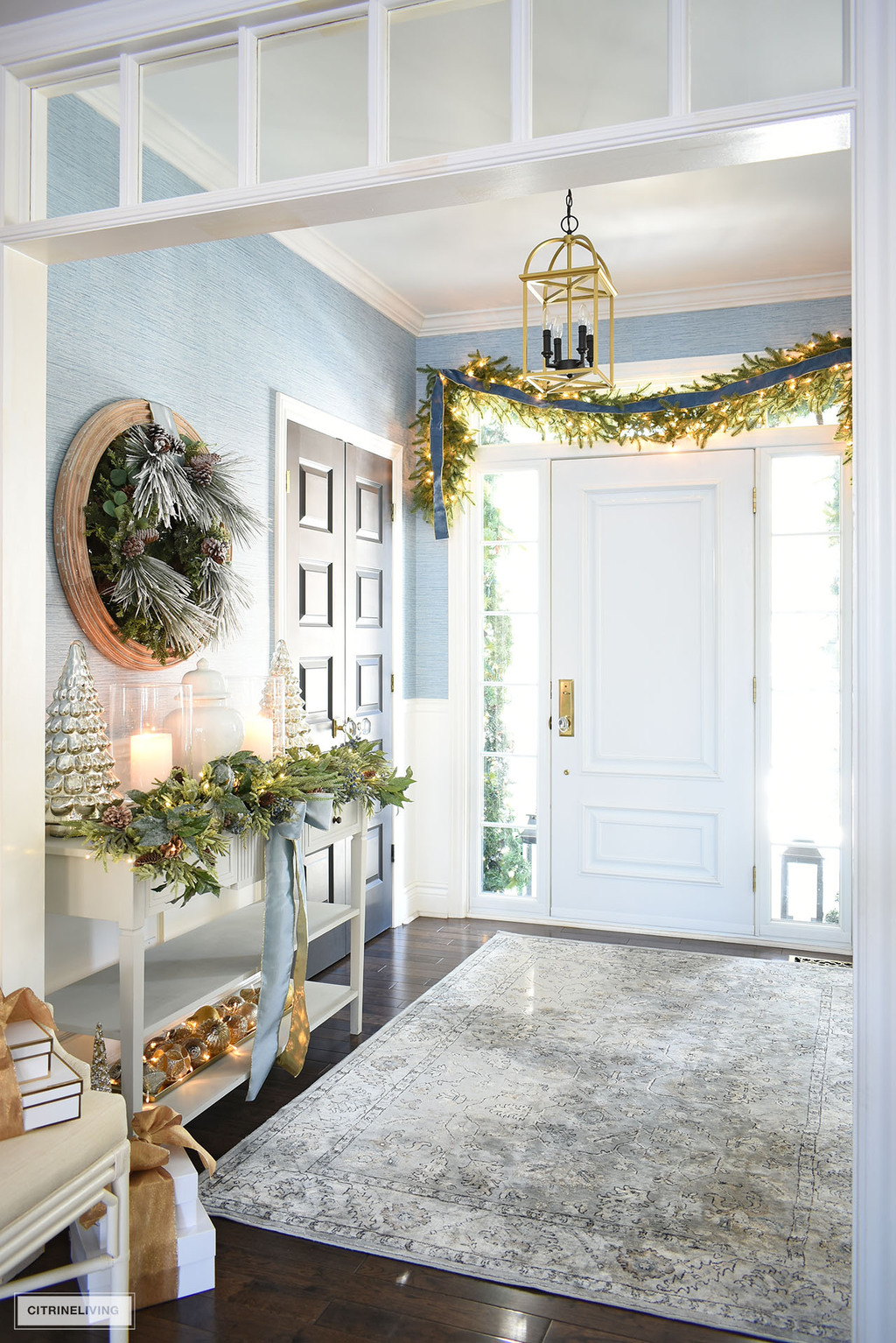 Christmas entryway decorated with greenery, garland and blue ribbons.