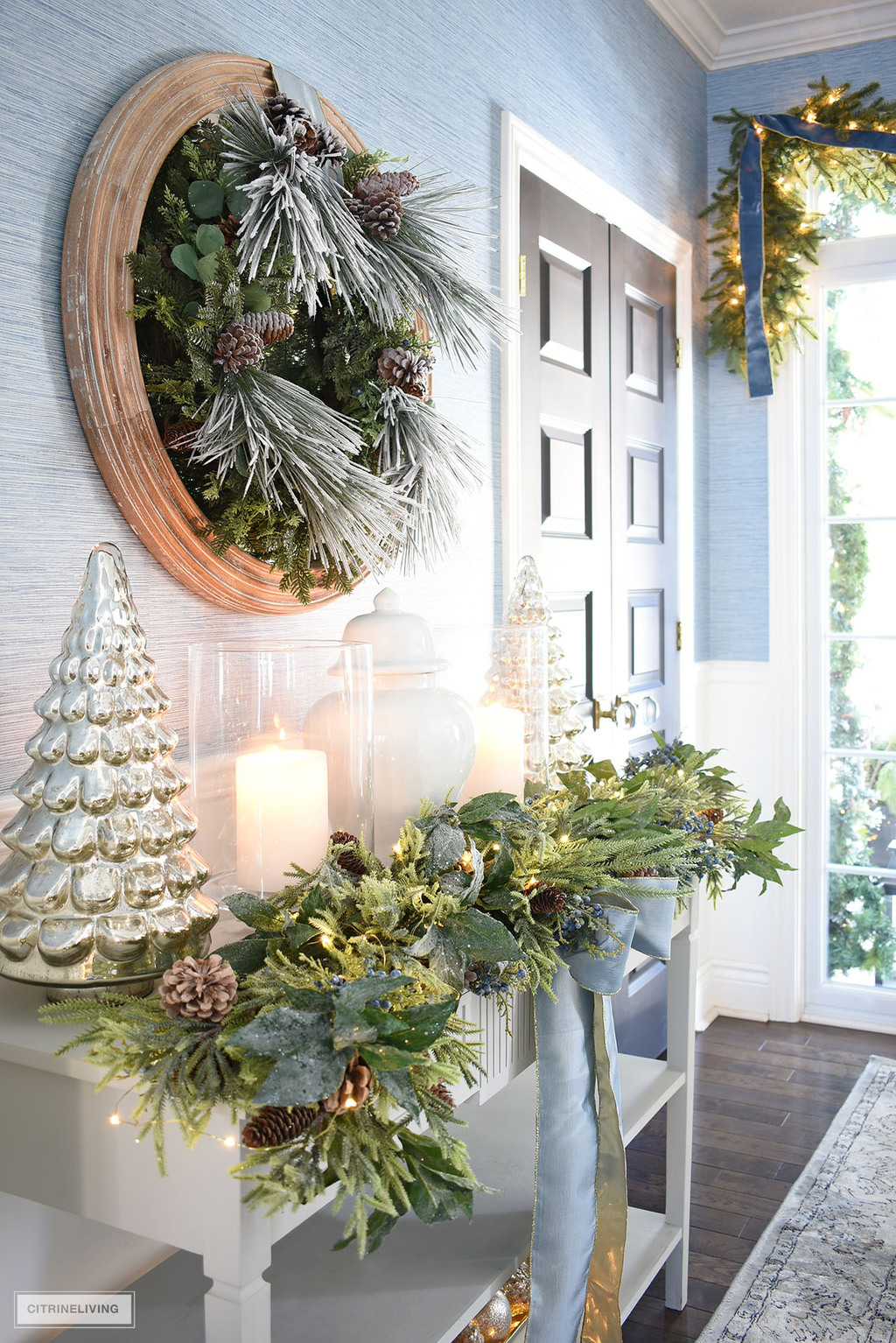 Christmas decorated entryway table with lush greenery, mercury glass trees, hurricane lanterns.