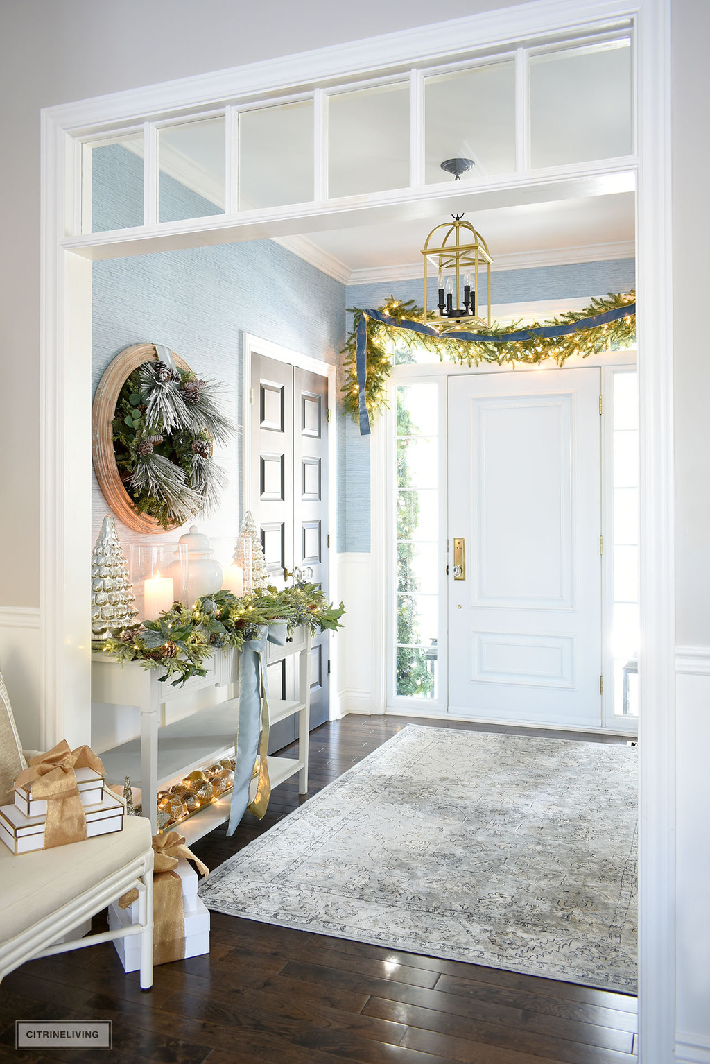 Elegant Christmas entryway decorated with greenery, garlands and blue ribbon.