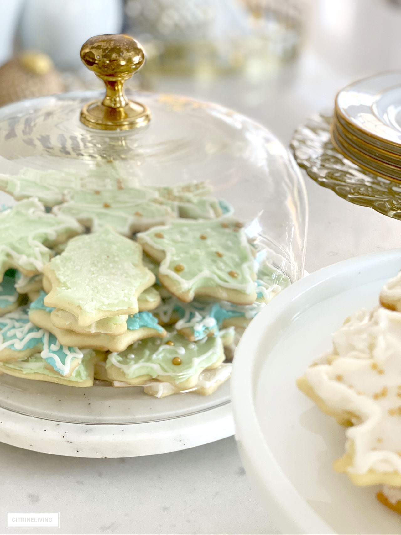 Cake stand with marble base and glass top filled with beautiful mint green and turquoise frosted Christmas cookies.