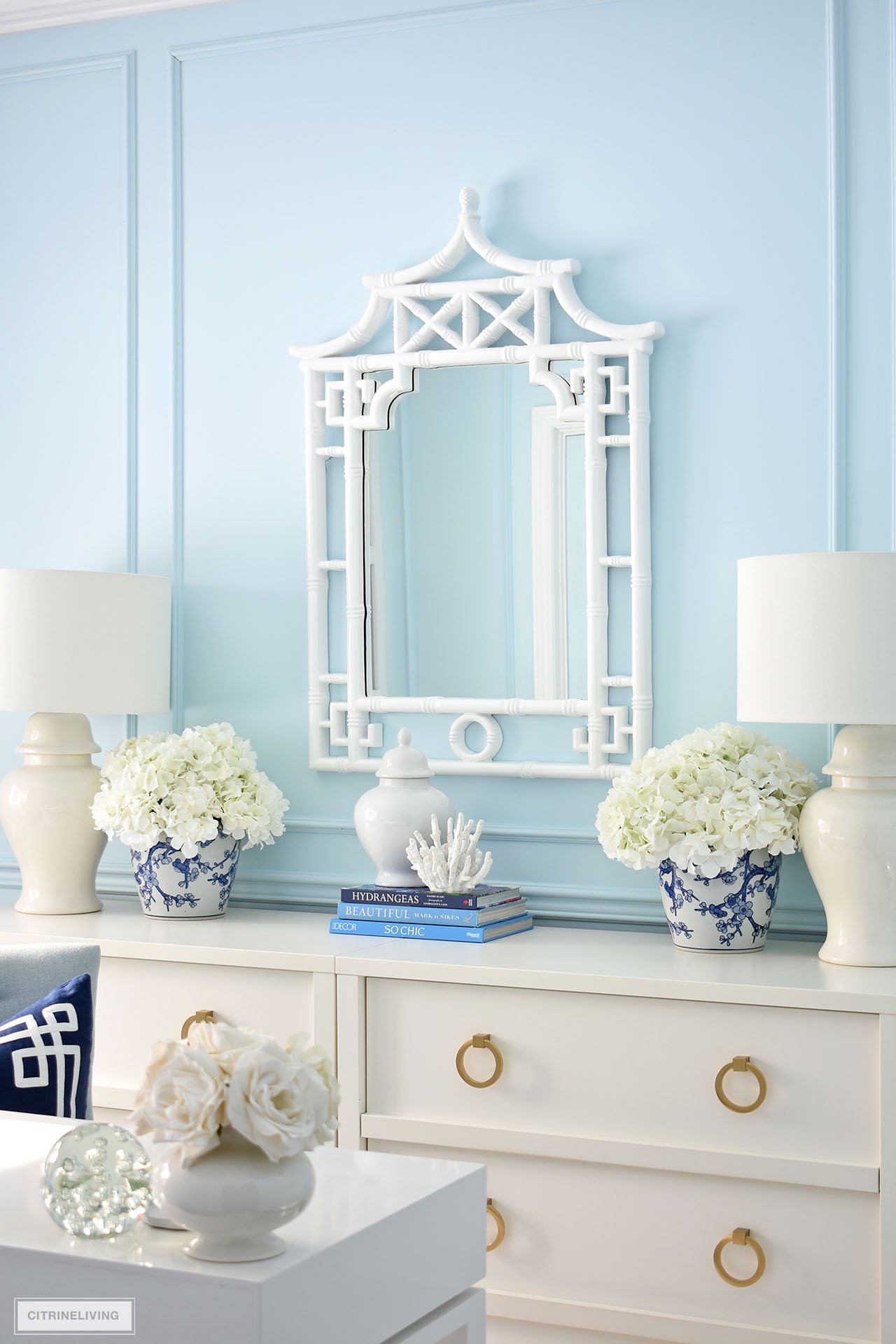 Pagoda mirror flanked by faux white hydrangeas in blue and white planters.