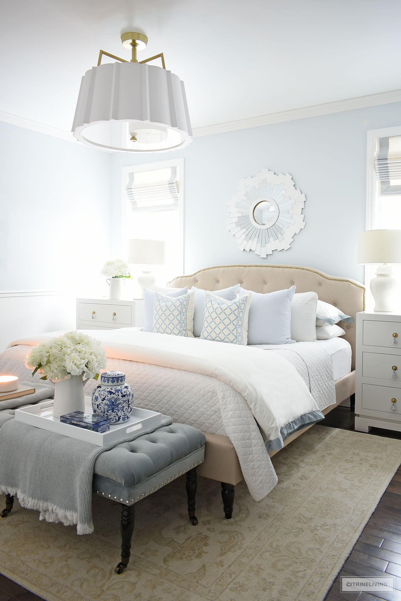 Gorgeous and calming winter bedroom decorated with soft layers of white quilted bedding and soft blue throw pillows, with a chic blue upholstered bench at the foot of the bed.