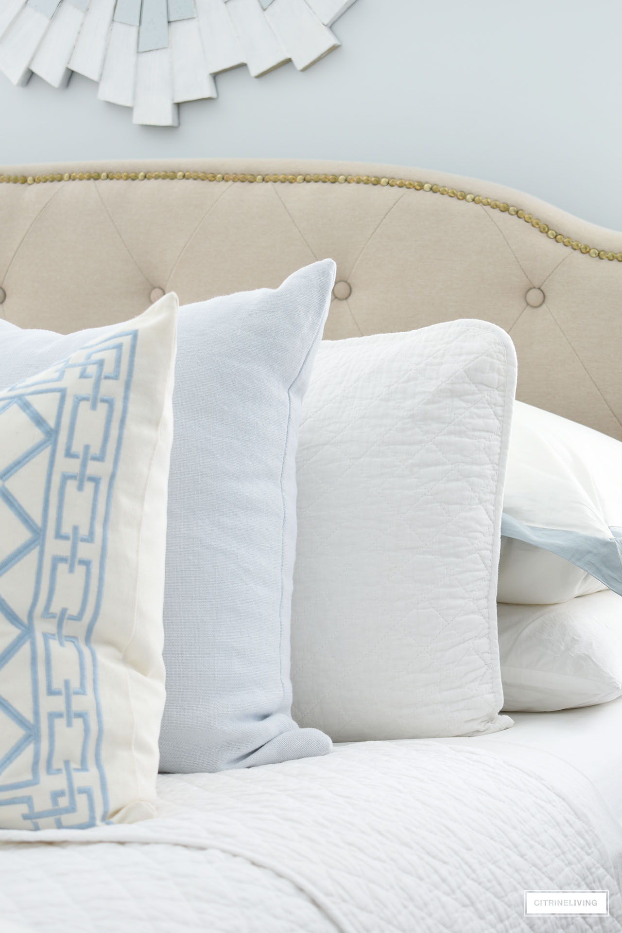 Layers of quilted bedding, white sheets and light blue throw pillows.