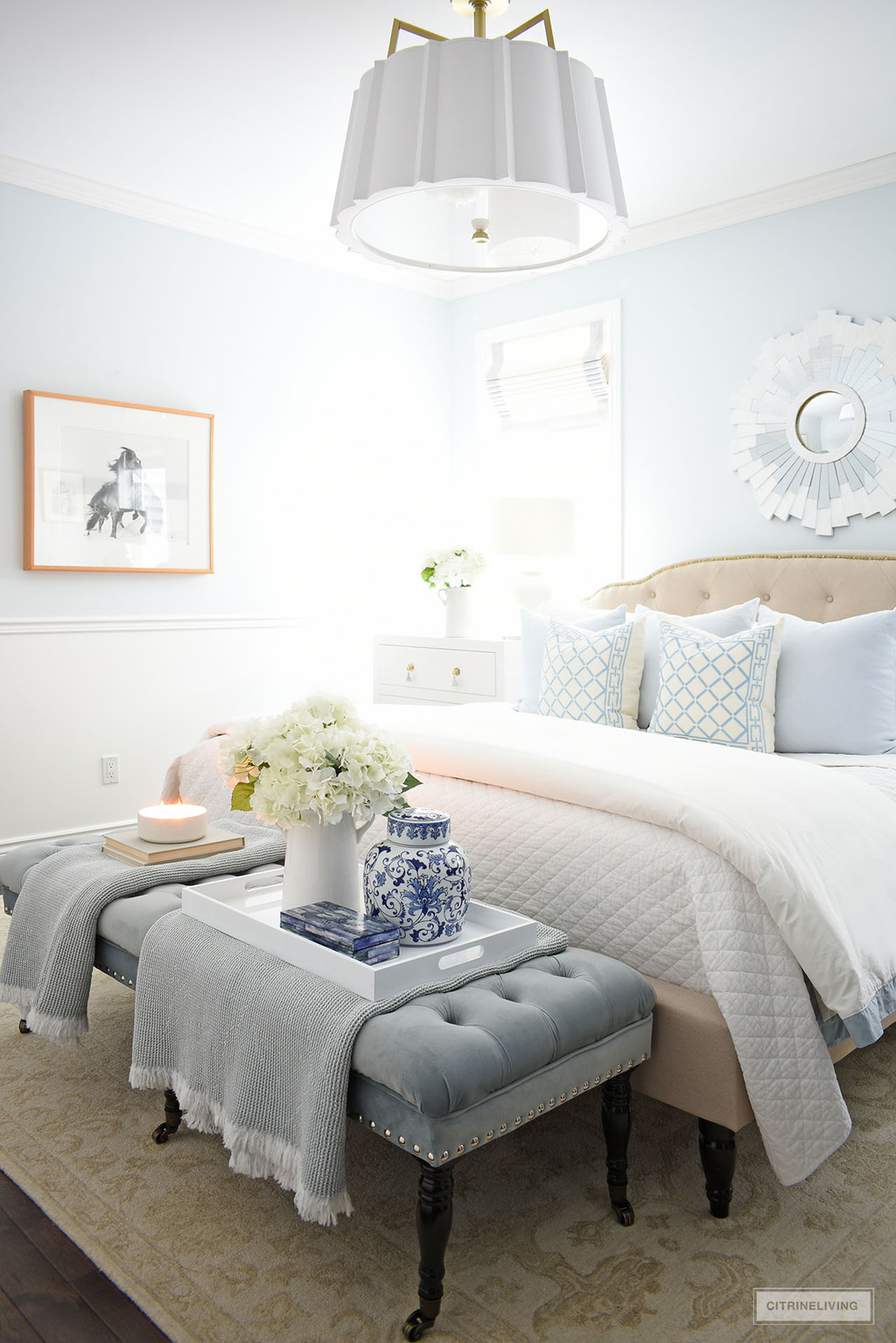 Gorgeous winter bedroom decorating with layers of white quilted bedding light blue and white pillows, and a beautiful upholstered bench at the foot of the bed with pretty accessories.