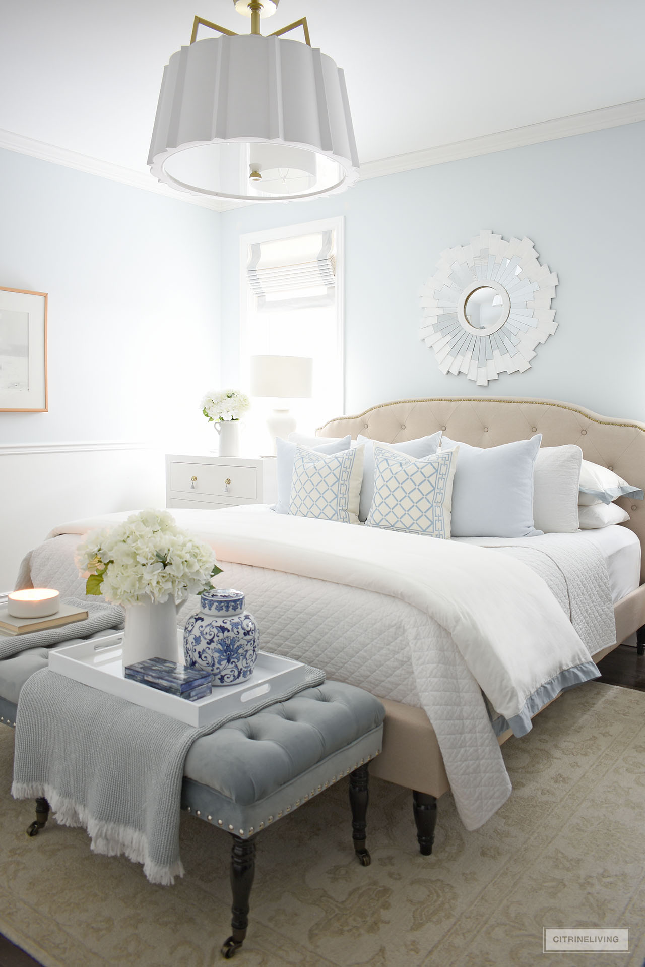 Beautiful calming bedroom with layers of white bedding, light blue throw pillows, throws, candles and faux flowers.