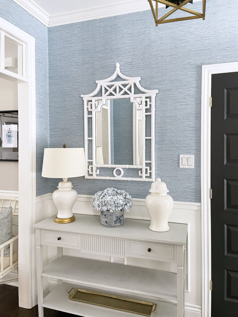 Entryway with blue wallpaper and white pagoda mirror, console table with ginger jar lamp, ginger jar, planter with light blue hydrangeas.
