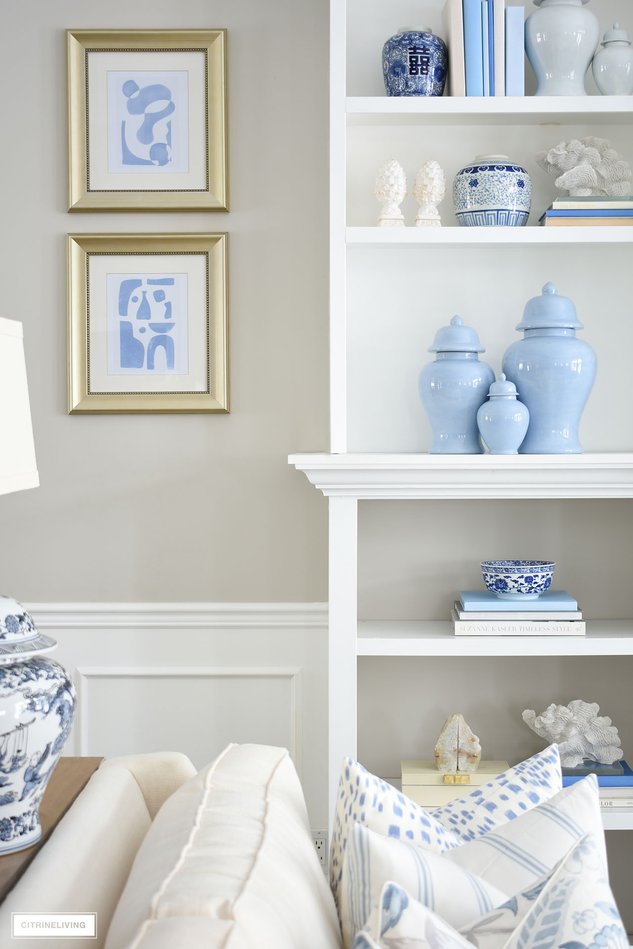 Bookshelves styled for spring in varying shades of blue, with white accents, flanked by modern art in gold frames.