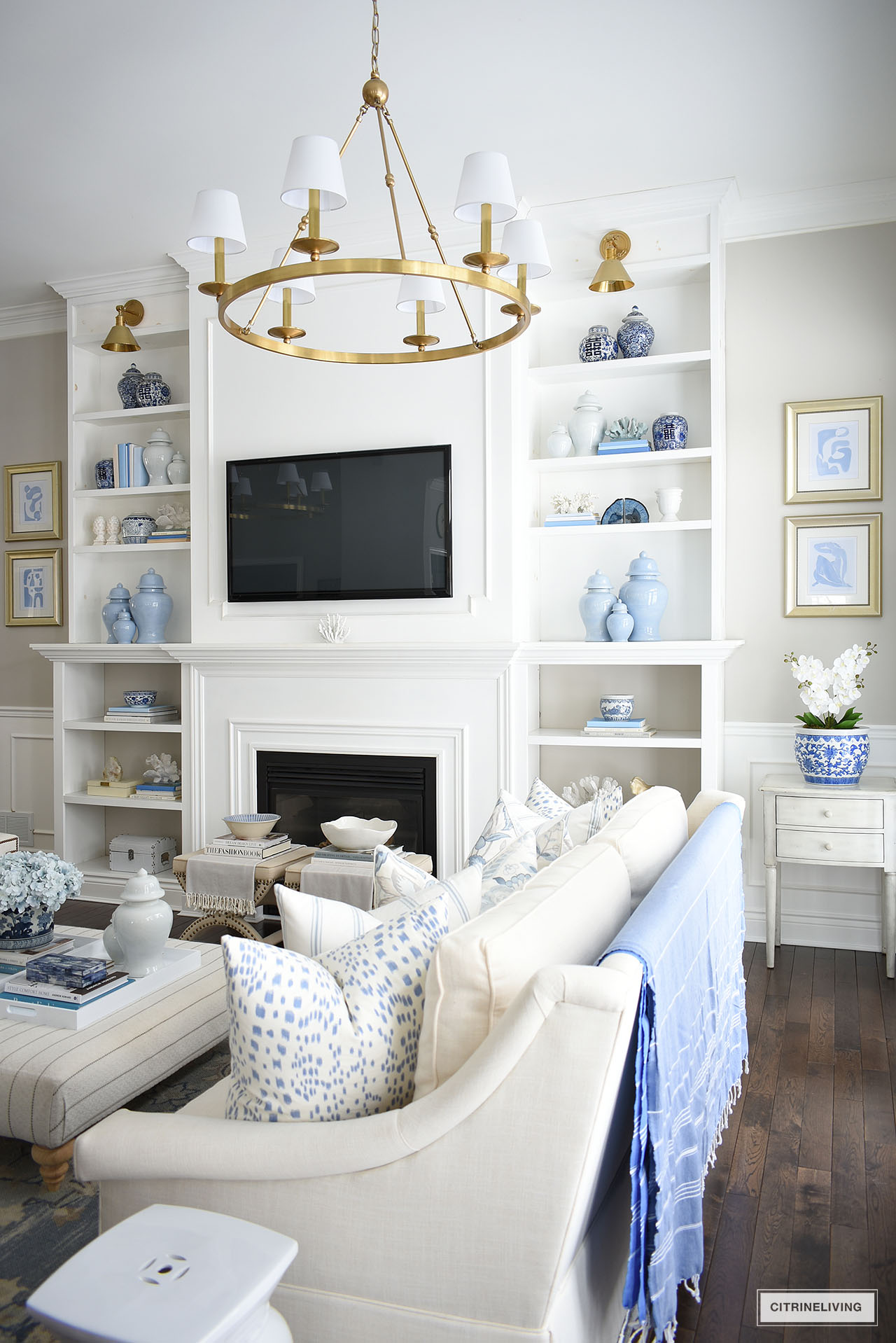 Gorgeous living room spring decor and bookshelves dressed in a collection of blue and white ginger jars, collared books, coral sculptures and objects, styled with a curated look.