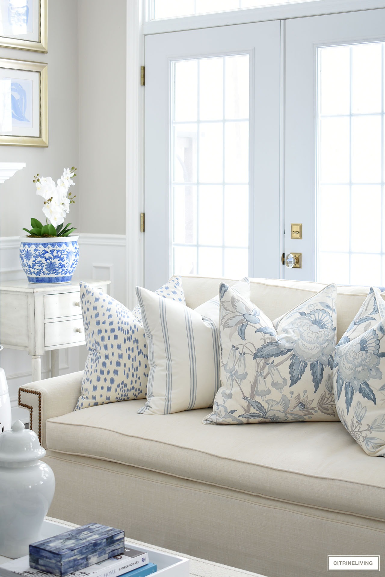 Blue and white pillows for spring arranged on a white sofa, a beautiful orchid arranged in a blue and white chinoiserie planter are elegant for spring.